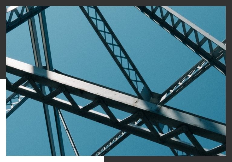 A low-angle, upward view of a complex steel truss structure against a clear blue sky.
