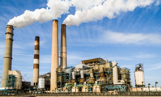 Industrial power plant with multiple striped smokestacks emitting white steam against a blue sky with some clouds.
