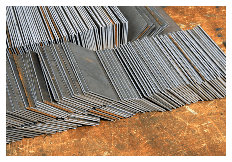 Stack of polished metal sheets resting on a workbench in a dimly lit industrial warehouse setting.
