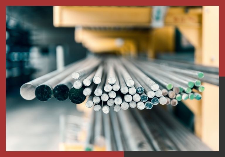 Close-up of metal rod inventory on a warehouse rack, showing color-coded ends used to distinguish between different steel or aluminum alloys and tempers.